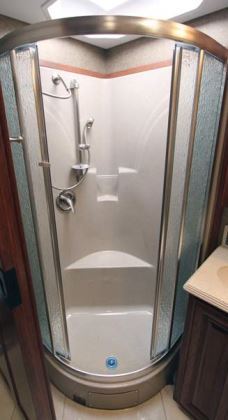 The bathroom features a molded fiberglass shower enclosure with a sliding circular rain glass door.
