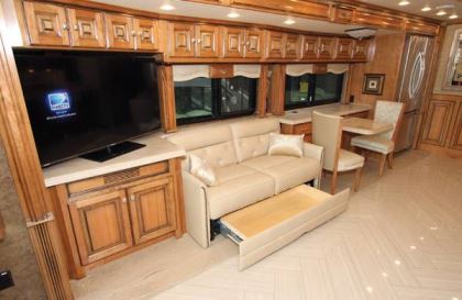 The 45LP's front curbside slideout encompasses an entertainment center with a 50-inch LED TV on one end, followed by a sofa bed, a dinette, and a residential refrigerator.