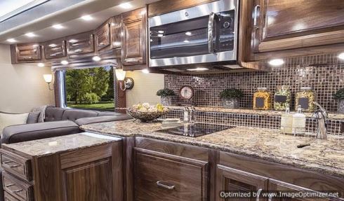 The curbside of the galley in the Realm LV-3 floor plan includes an electric cooktop, a drawer-style dishwasher below it, and a convection-microwave oven, plus plentiful work space on the quartz countertops. 