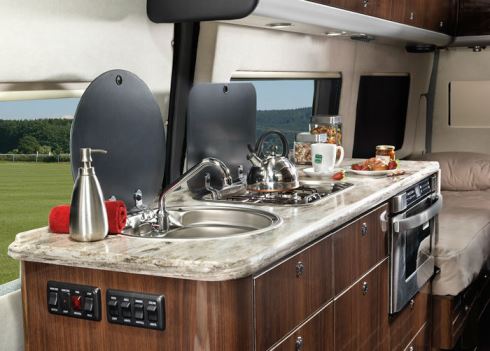 The Grand Tour's curbside galley features a sink and a two-burner cooktop, with smoked-glass covers, which are built into a Corian countertop. Beneath the counter is a 1.2-cubic-foot drawer-style microwave overn.