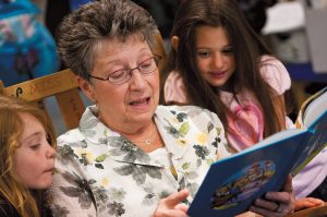 A foster grandparent volunteer reads to girls at school.