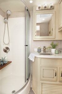 The bath holds a fiberglass shower with curved glass doors and a vanity with a stainless-steel sink.