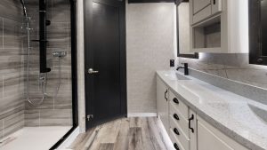 In the bathroom, the 48-inch shower features a residential rain showerhead and sprayer; the vanity includes two sinks.